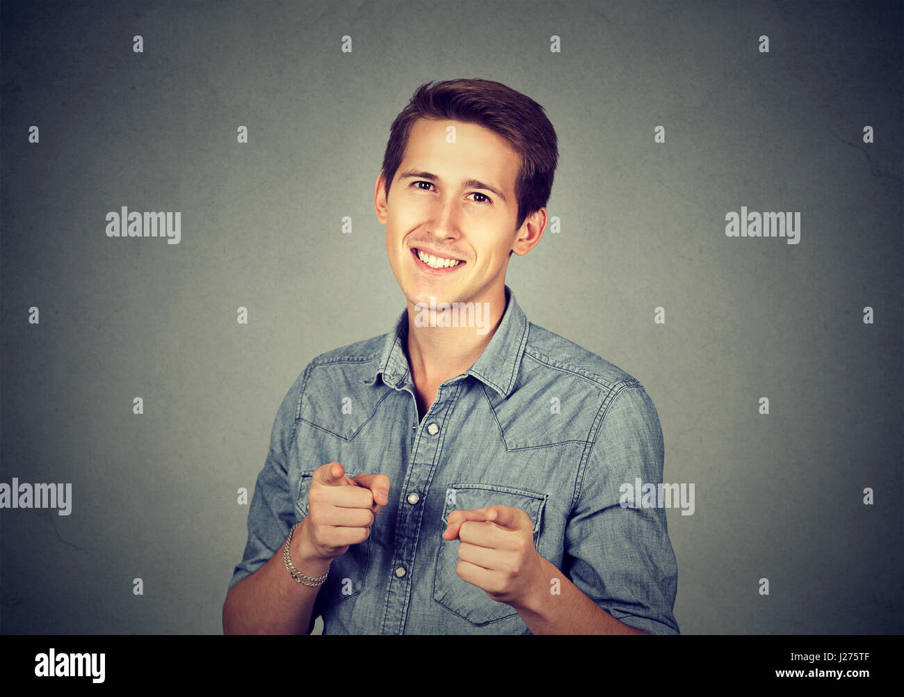 Portrait handsome young smiling man giving thumbs up pointing fingers at camera, picking you as friend isolated on grey wall background. Positive huma Stock Photo