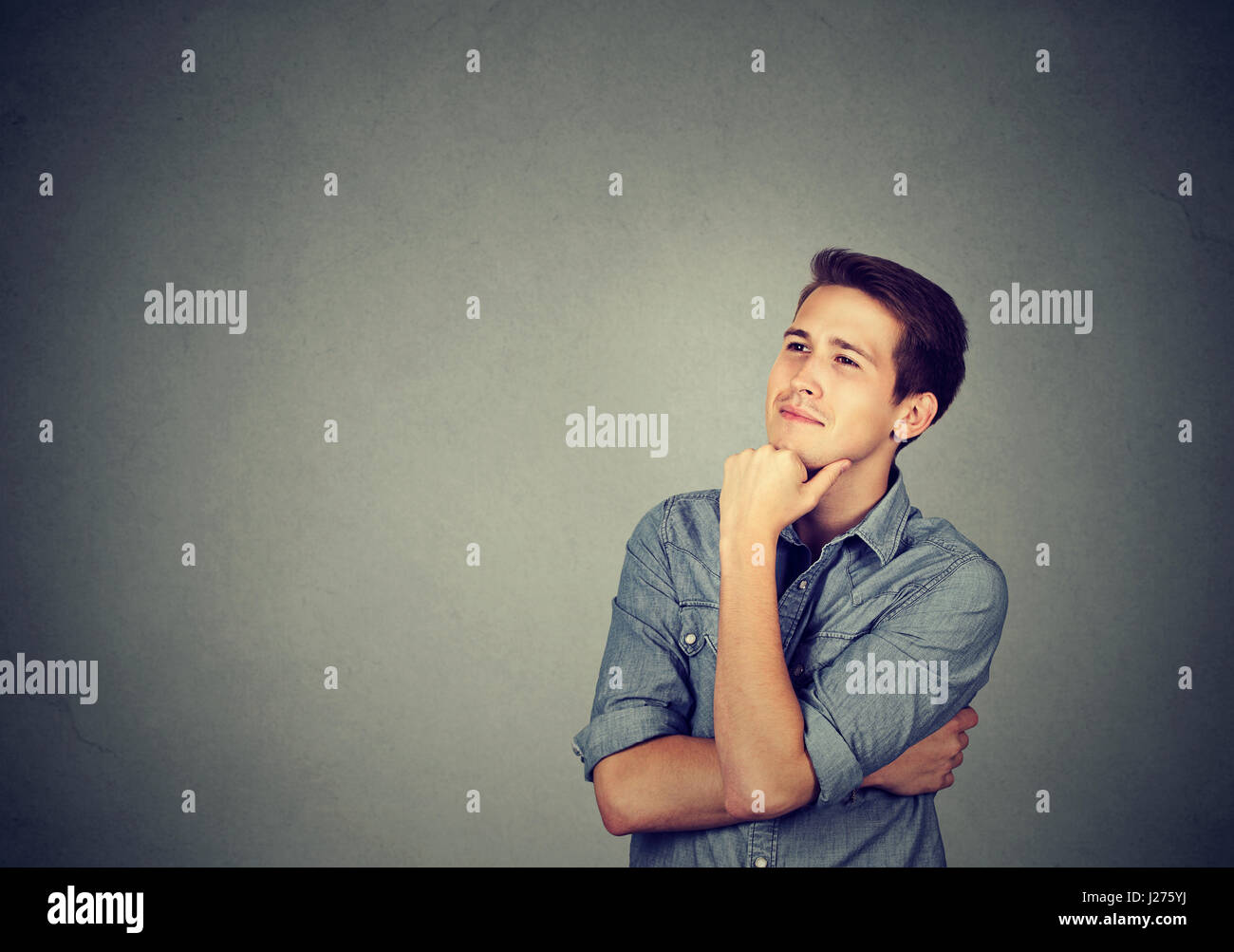 Happy young man thinking daydreaming looking up isolated on gray wall background Stock Photo