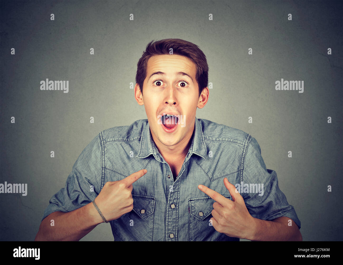 young happy surprised man pointing at himself you mean me isolated on gray background. Human emotion facial expression feeling Stock Photo