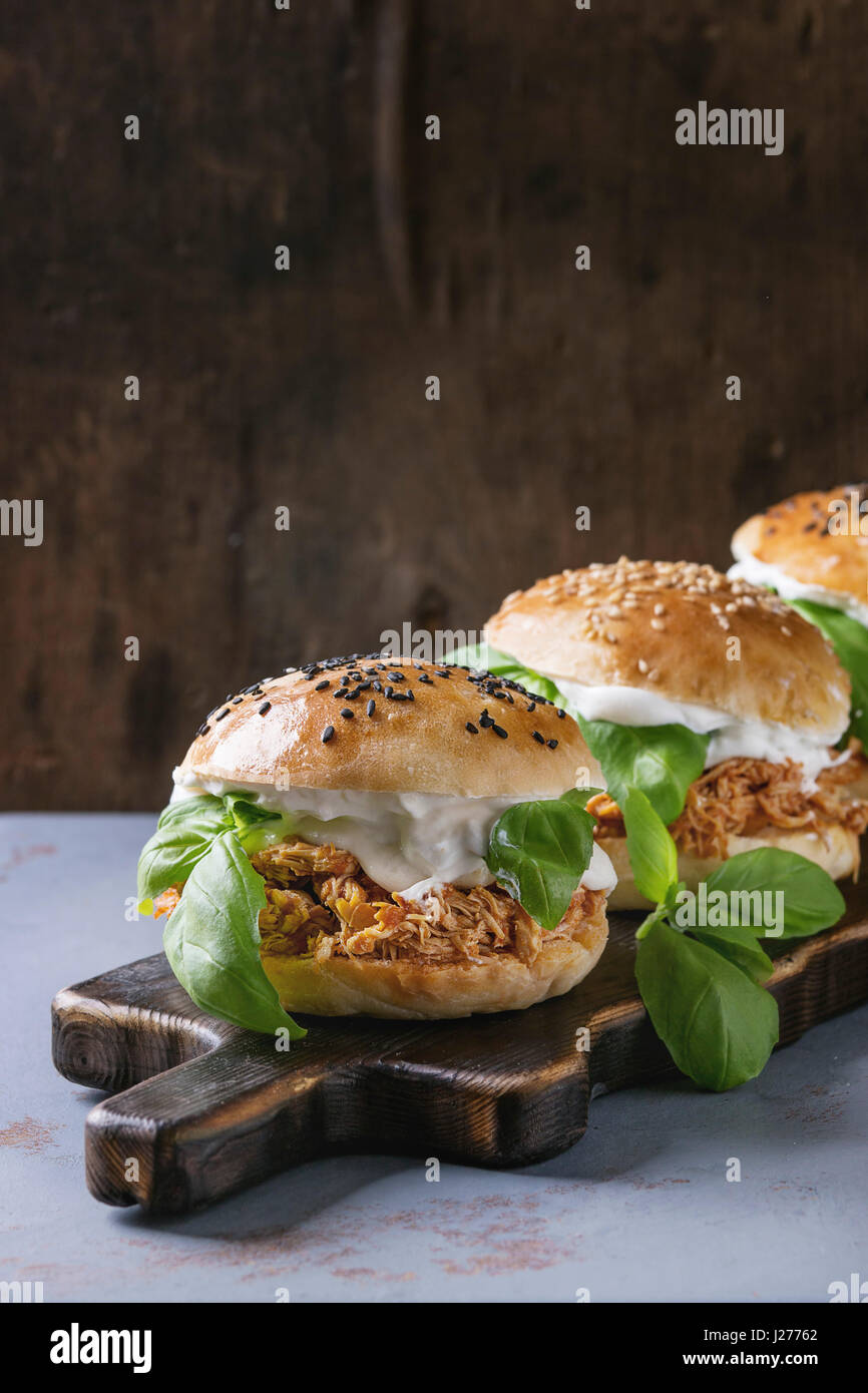 Homemade mini burgers with pulled chicken, basil, mozzarella cheese and yogurt sauce on wooden serving board over gray texture background. Healthy fas Stock Photo