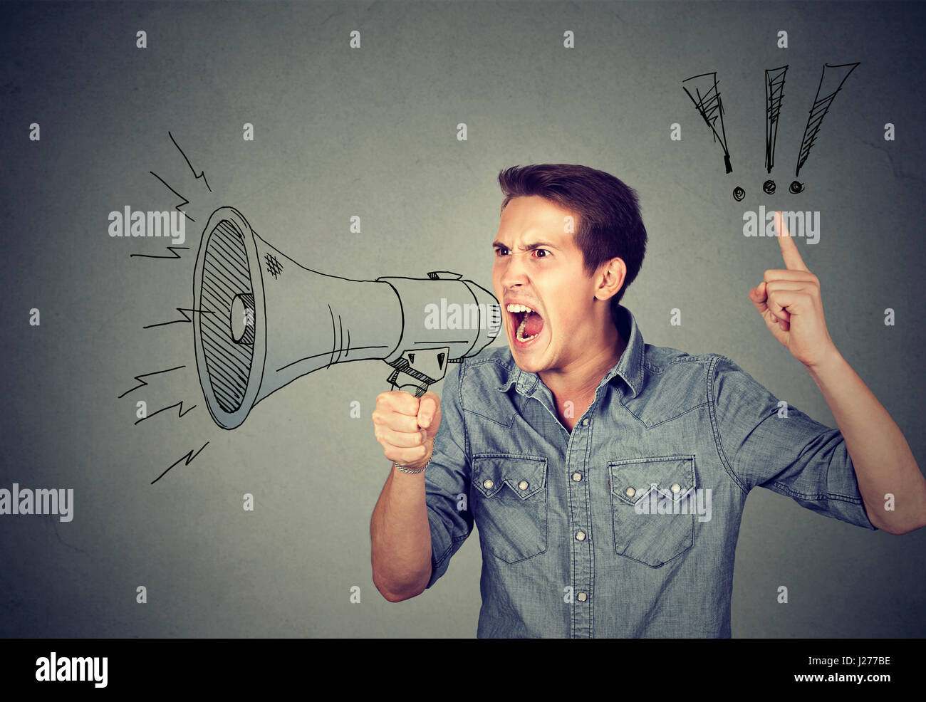 Side portrait angry young man holding screaming in megaphone isolated on gray background. Negative face expression emotion feeling. Propaganda, breaki Stock Photo