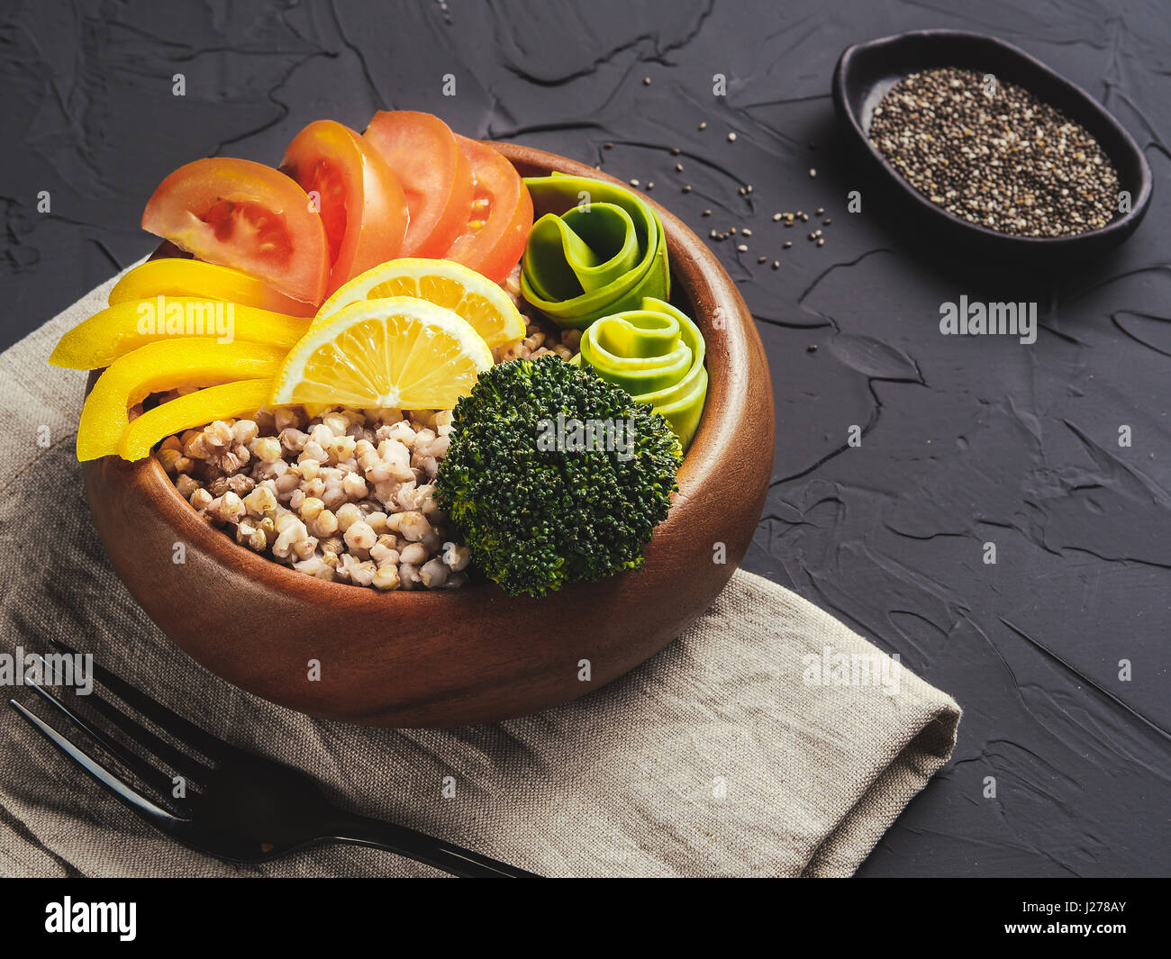 Close up view of vegetarian buddha bowl with green buckwheat, broccoli, avocado, tomatoes and yellow sweet pepper paprika on dark concrete background  Stock Photo