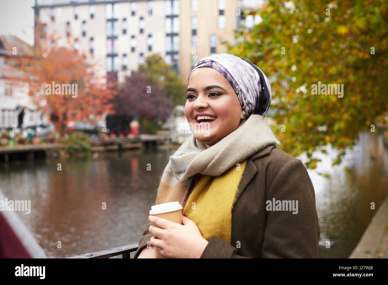 British Muslim Female With Takeaway Coffee By River In City Stock Photo