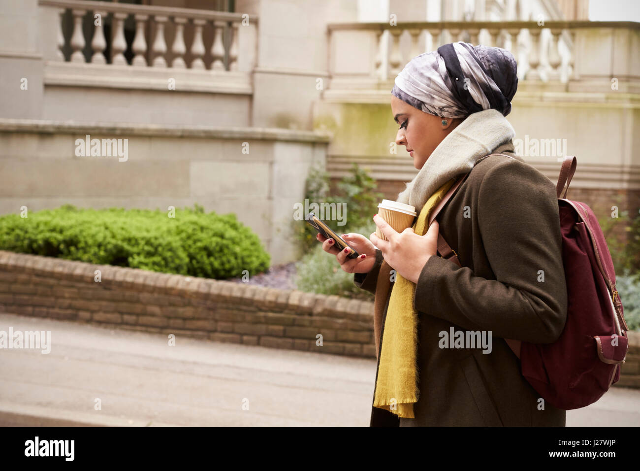 British Muslim Female Walks And Sends Text Message In City Stock Photo