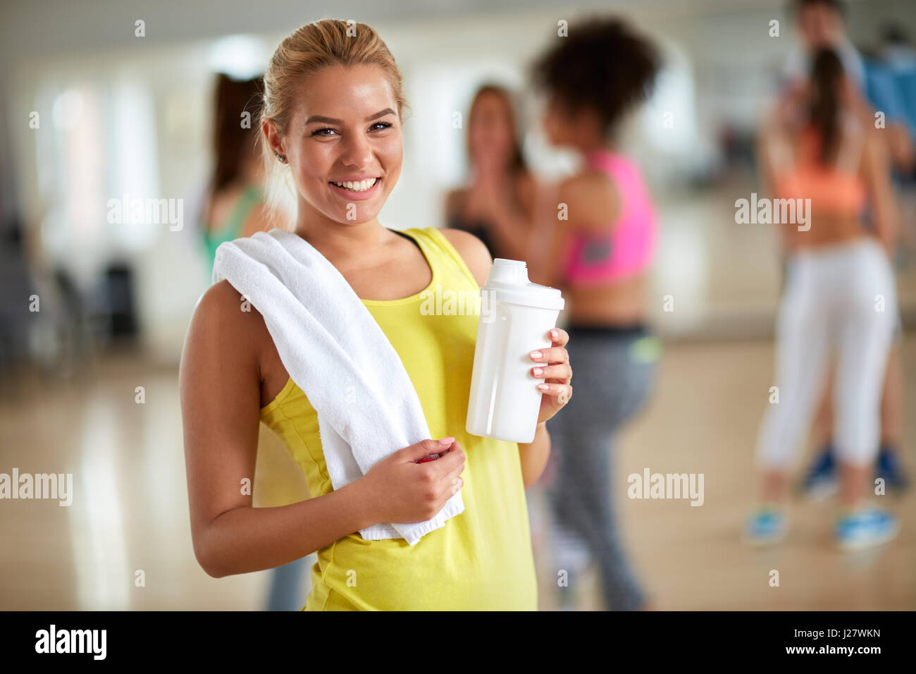 Cheerful young blond girl at gym after training with towel and bottle ...