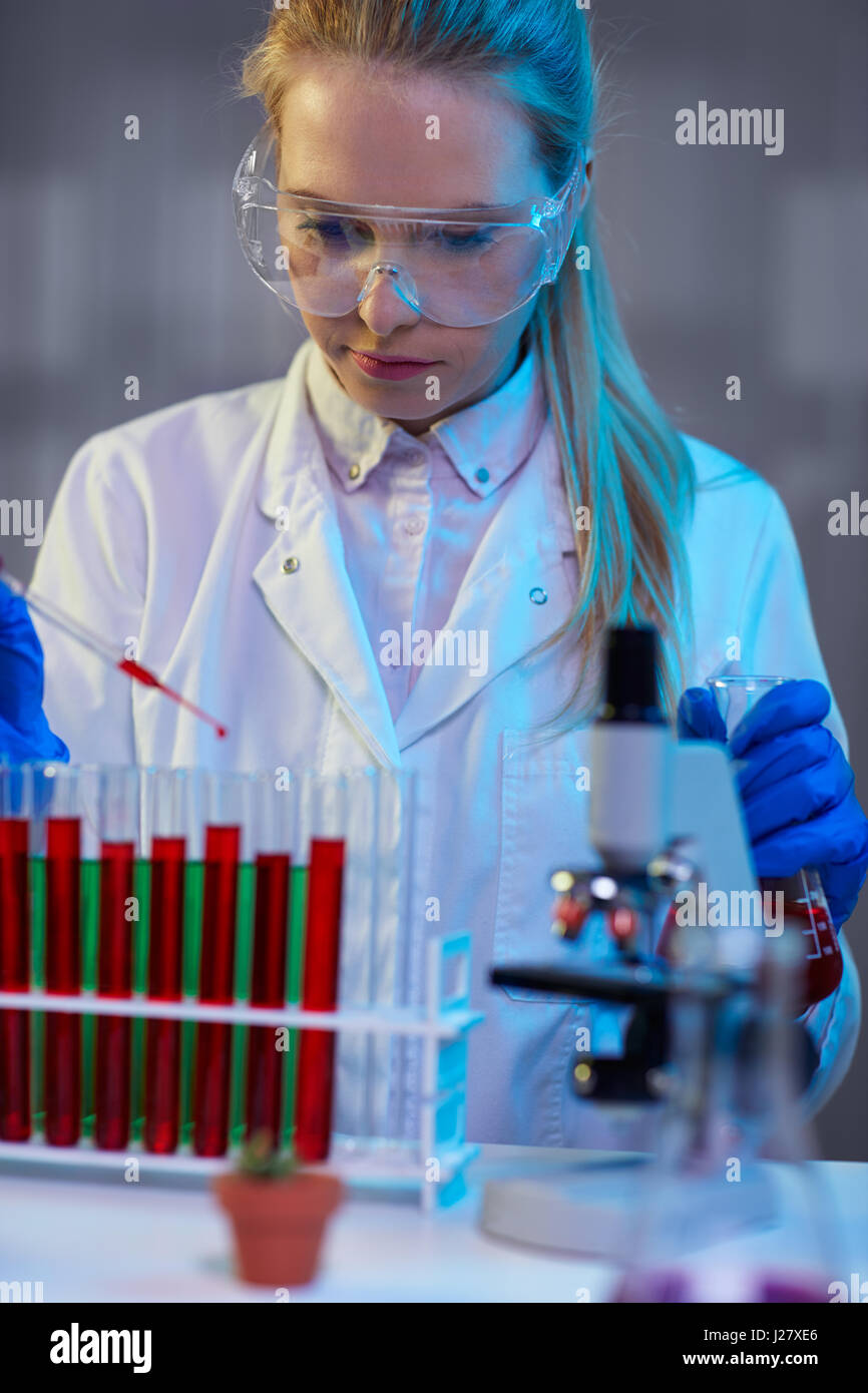 serious female chemical technician working at night in the lab with red liquid Stock Photo