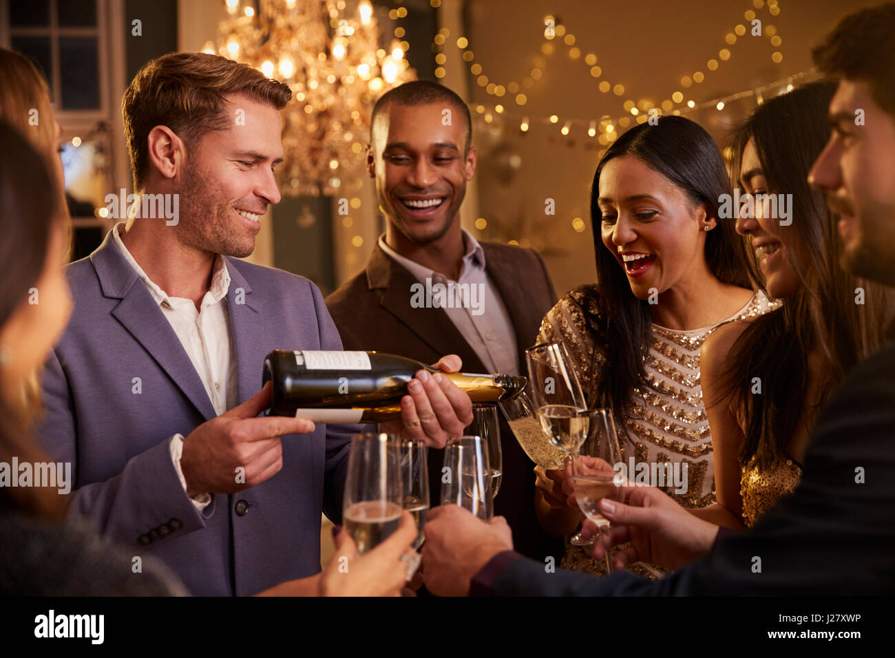 Friends Open Champagne As They Celebrate At Party Together Stock Photo