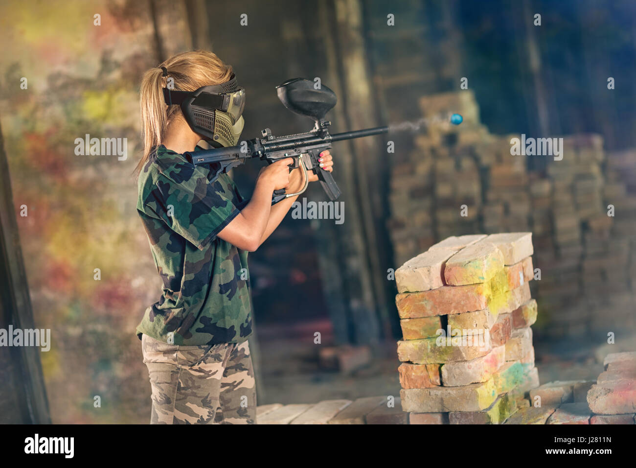 Female paintball gamer in action shooting on opposite team Stock Photo