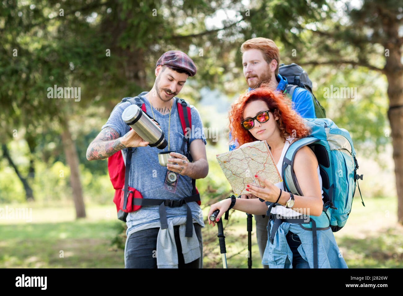 Sports people hiking with backpack, map, thermos and hiking sticks through forest Stock Photo