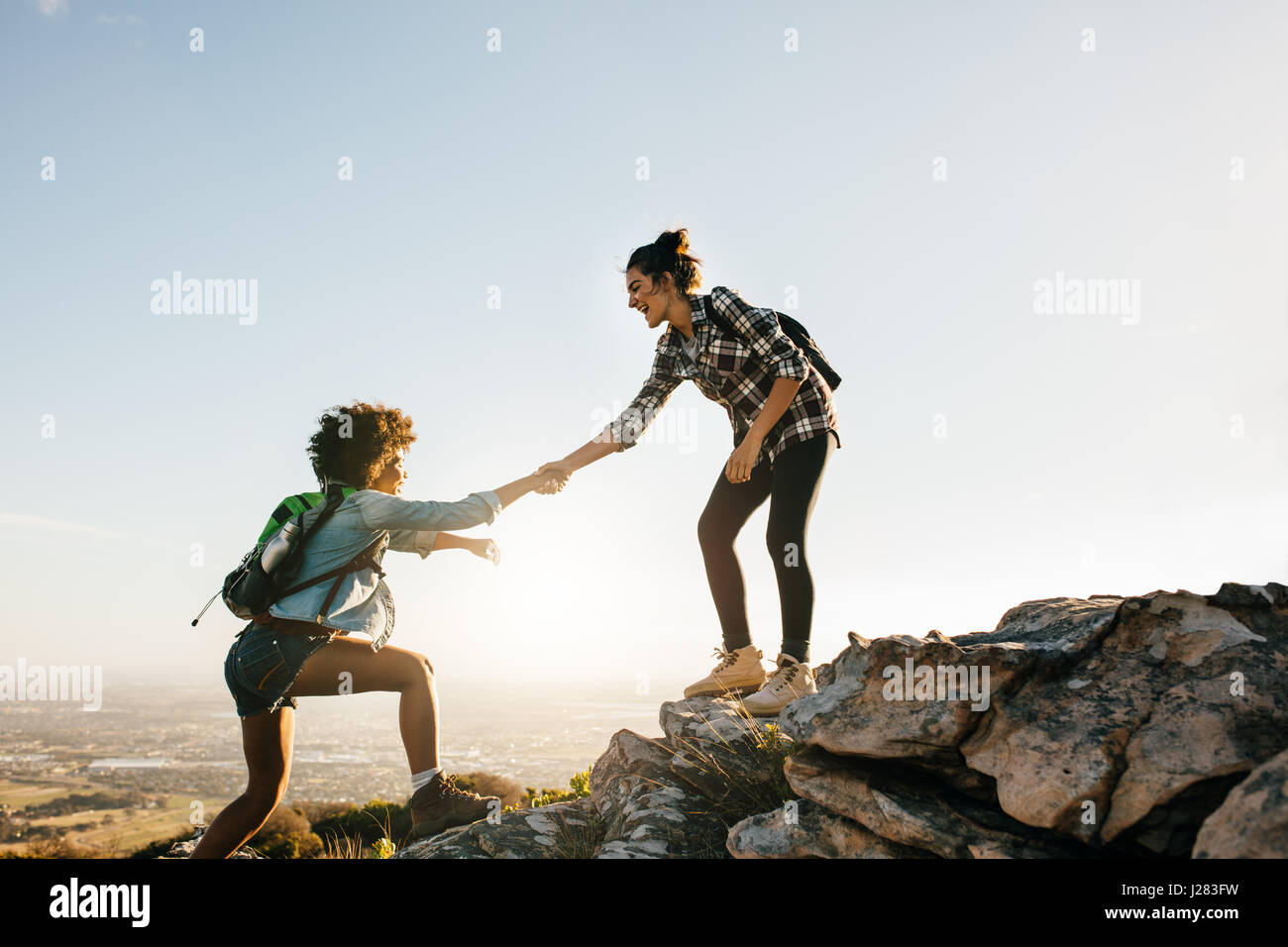 Young woman helping friend to climb up the rock. Two young females