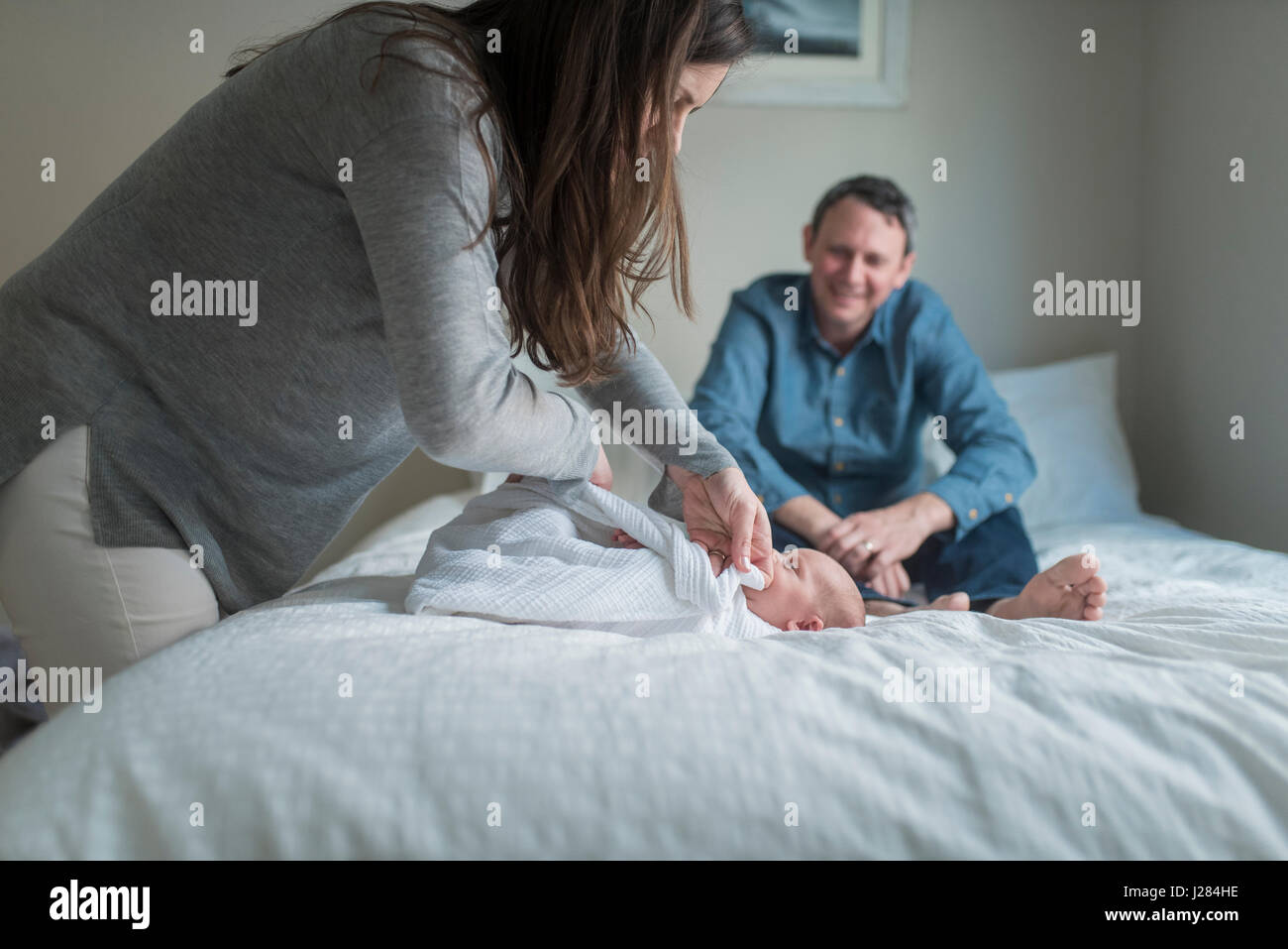 Side view of mother swaddling newborn baby boy with blanket while