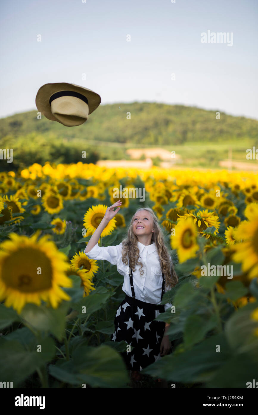 Happy teenage girl throwing cowboy hat on sunflower field Stock Photo