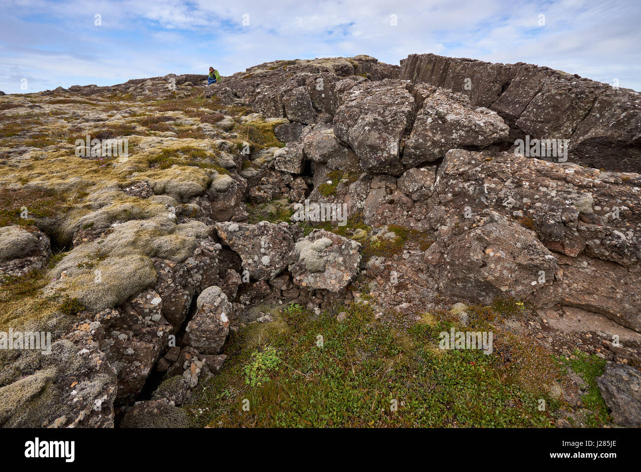 Person sitting on a massive rock formation just outside of Reykjavik, Iceland Stock Photo