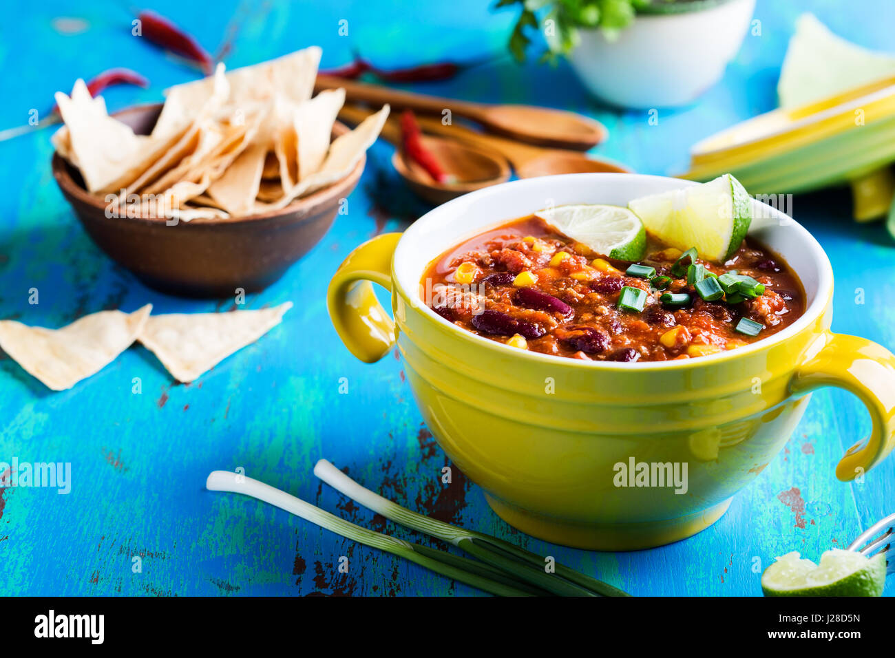 Chili con carne stew served in yellow bowl on rustic blue wooden table, Mexican cuisine Stock Photo