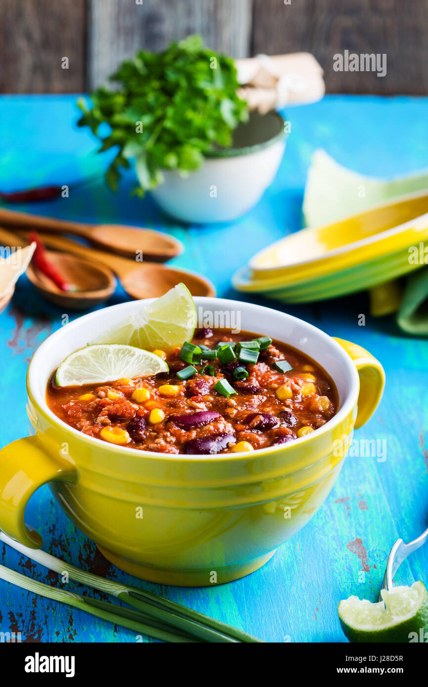 Chili con carne stew served in yellow bowl on rustic blue wooden table, Mexican cuisine Stock Photo