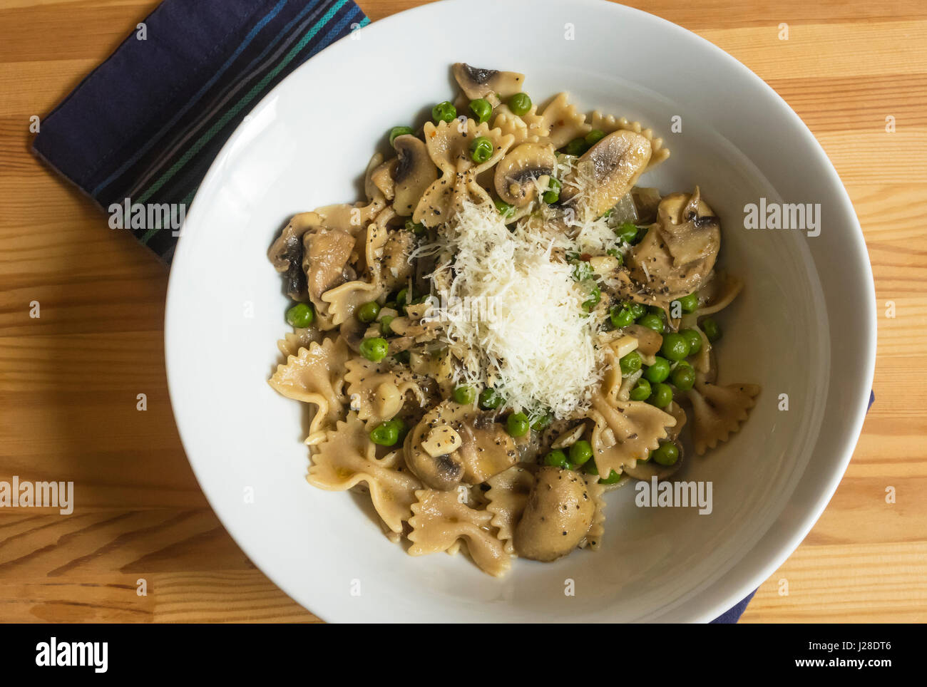 Bow tie pasta, with mushrooms, green peas and cheese in a white bowl