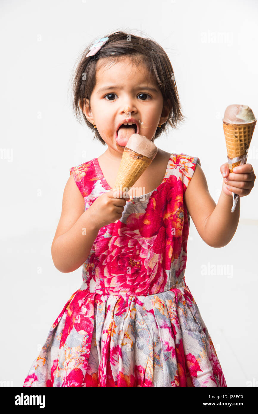 indian adorable infant or girl child licking or eating chocolate ice