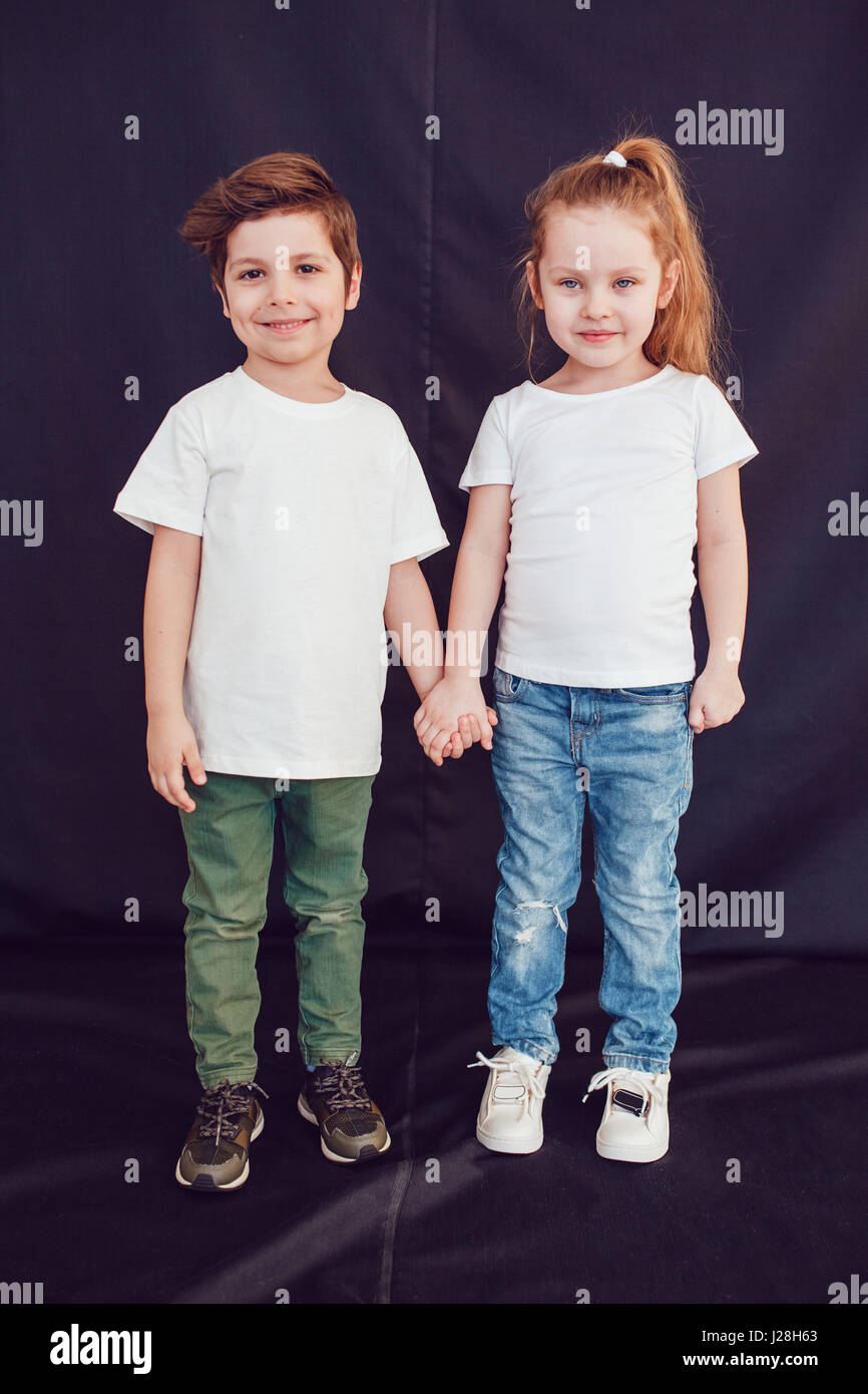 Two children in blank white t-shirts stand holding hands on black ...