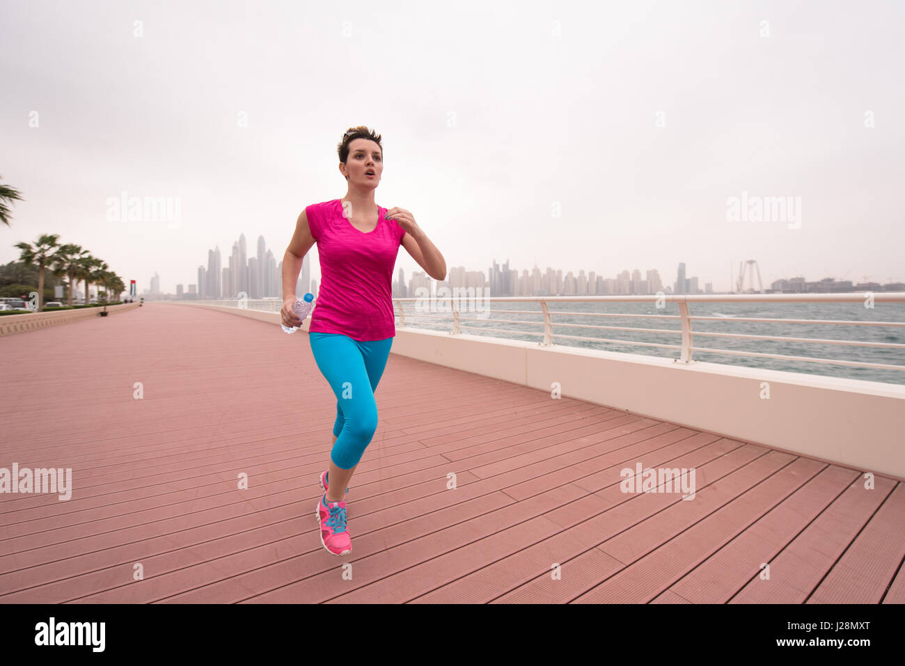 very active young beautiful woman busy running on the promenade along ...