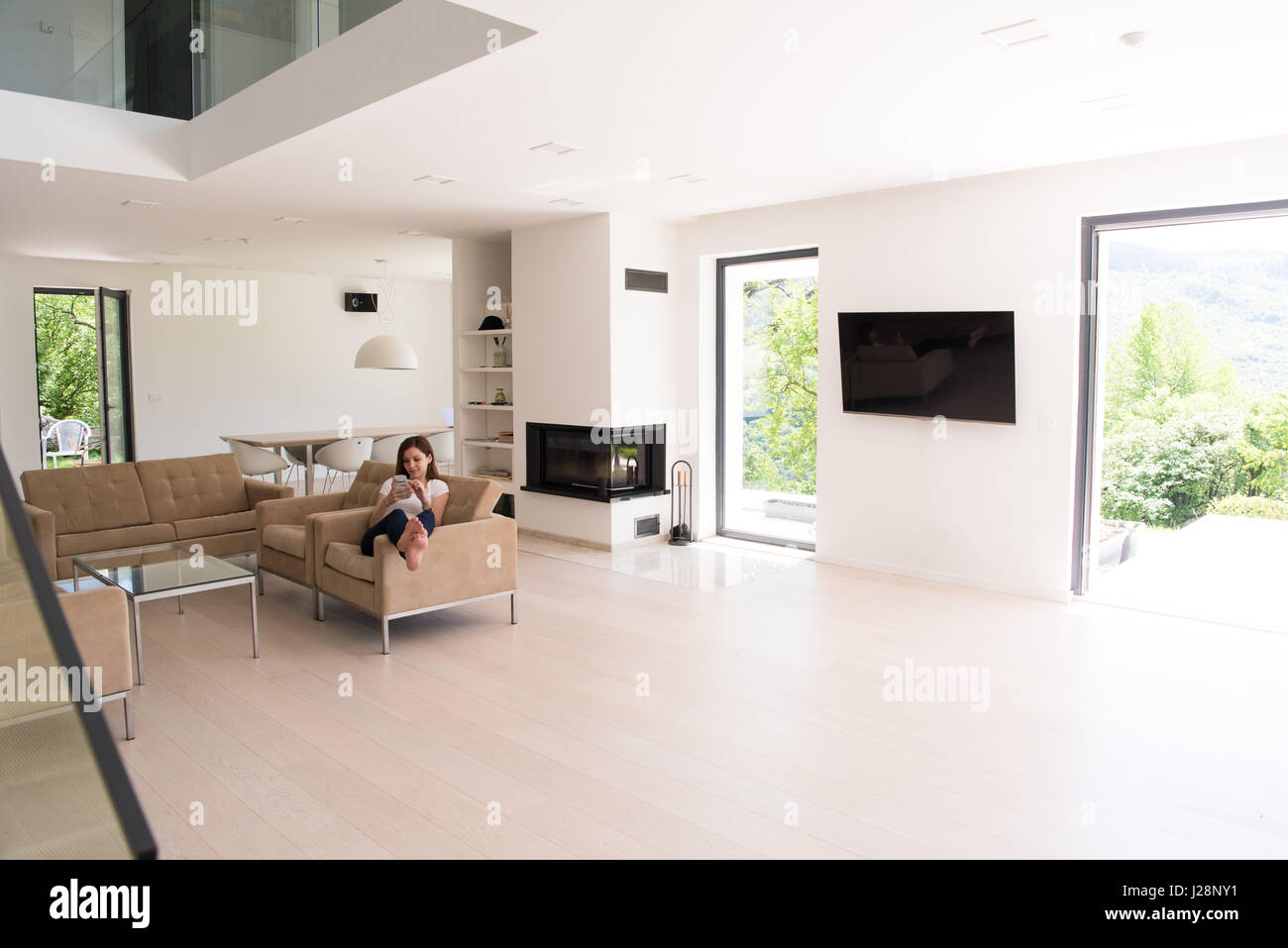 young happy woman sitting on sofa with mobile phone at luxury home ...