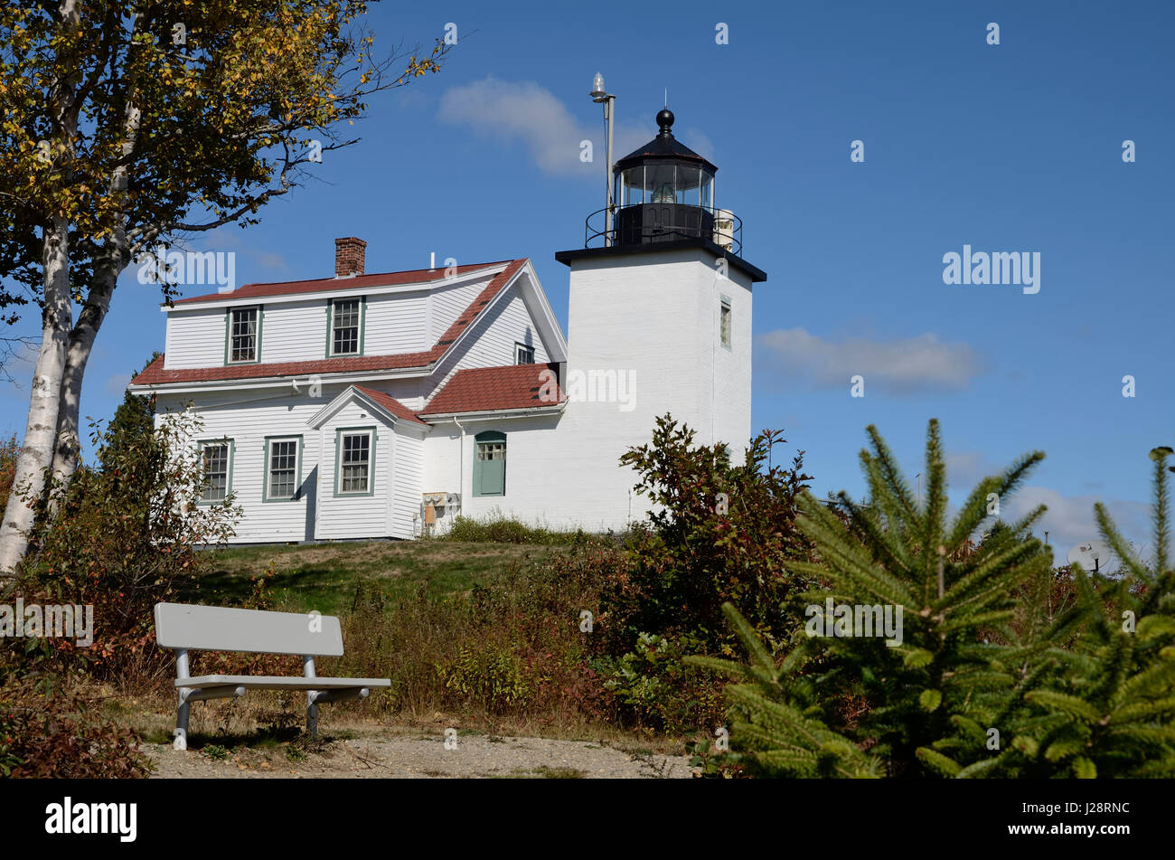 Fort Point Lighthouse on the Penobscot River near Stockton Springs, Maine.In the foreground there are a bench. Blue sky with 2 clouds. Stock Photo