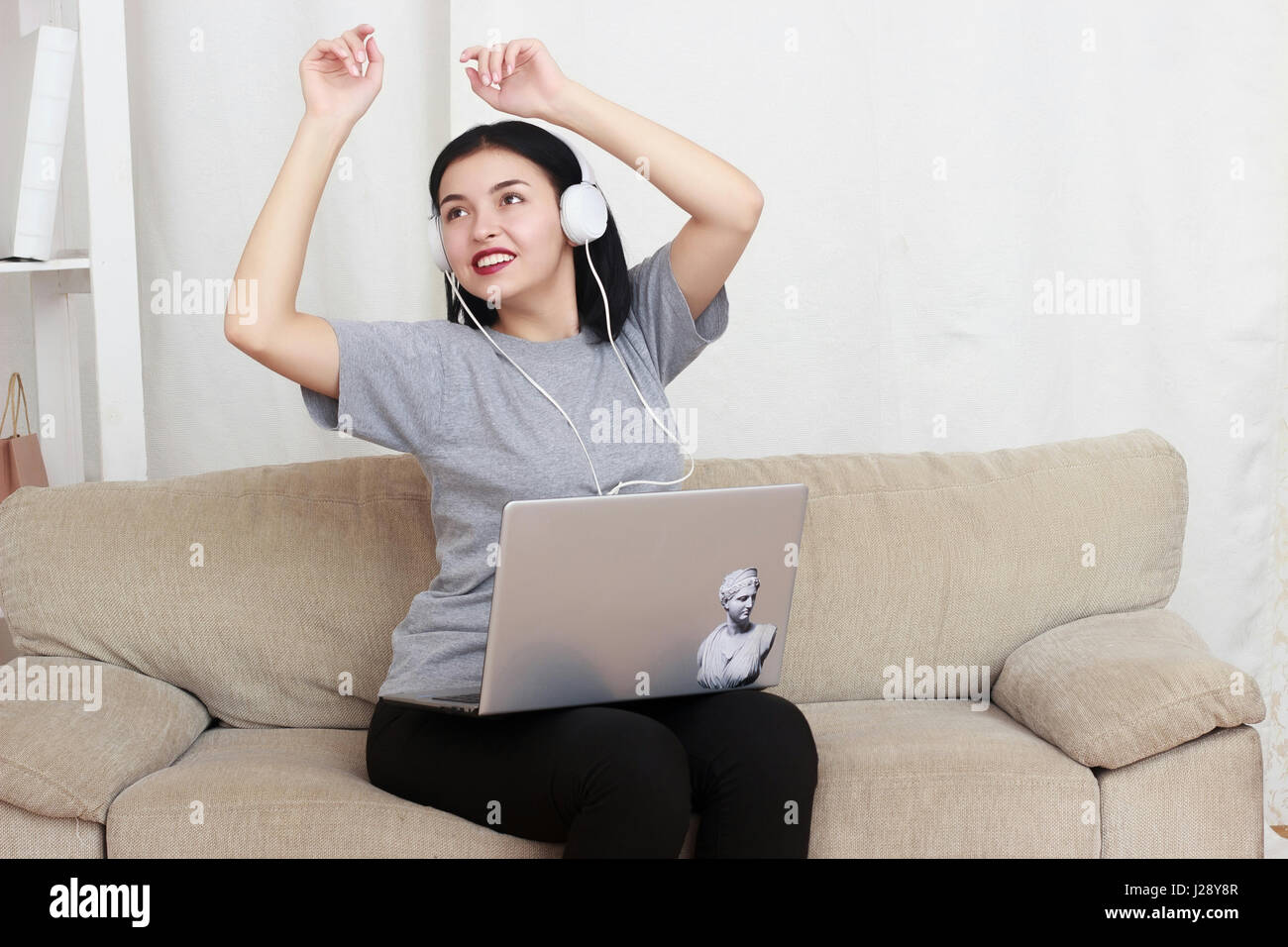 woman using laptop computer and headphones, sitting on living room Stock Photo