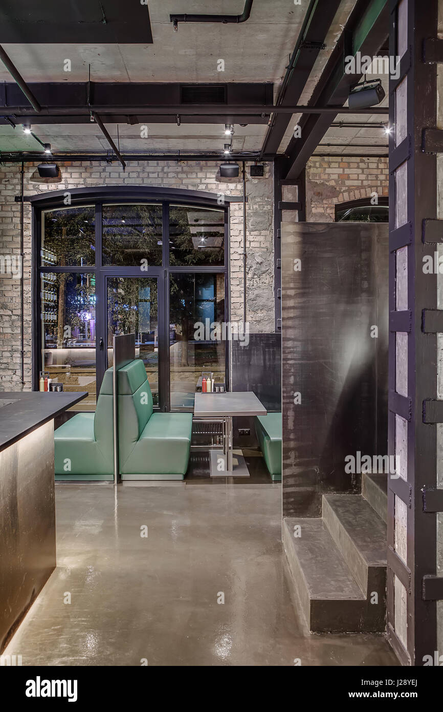 Interior in a loft style in a cafe with brick and concrete walls, glowing  lamps. There is a bar rack, stairway, green sofas with tables and  partitions Stock Photo - Alamy