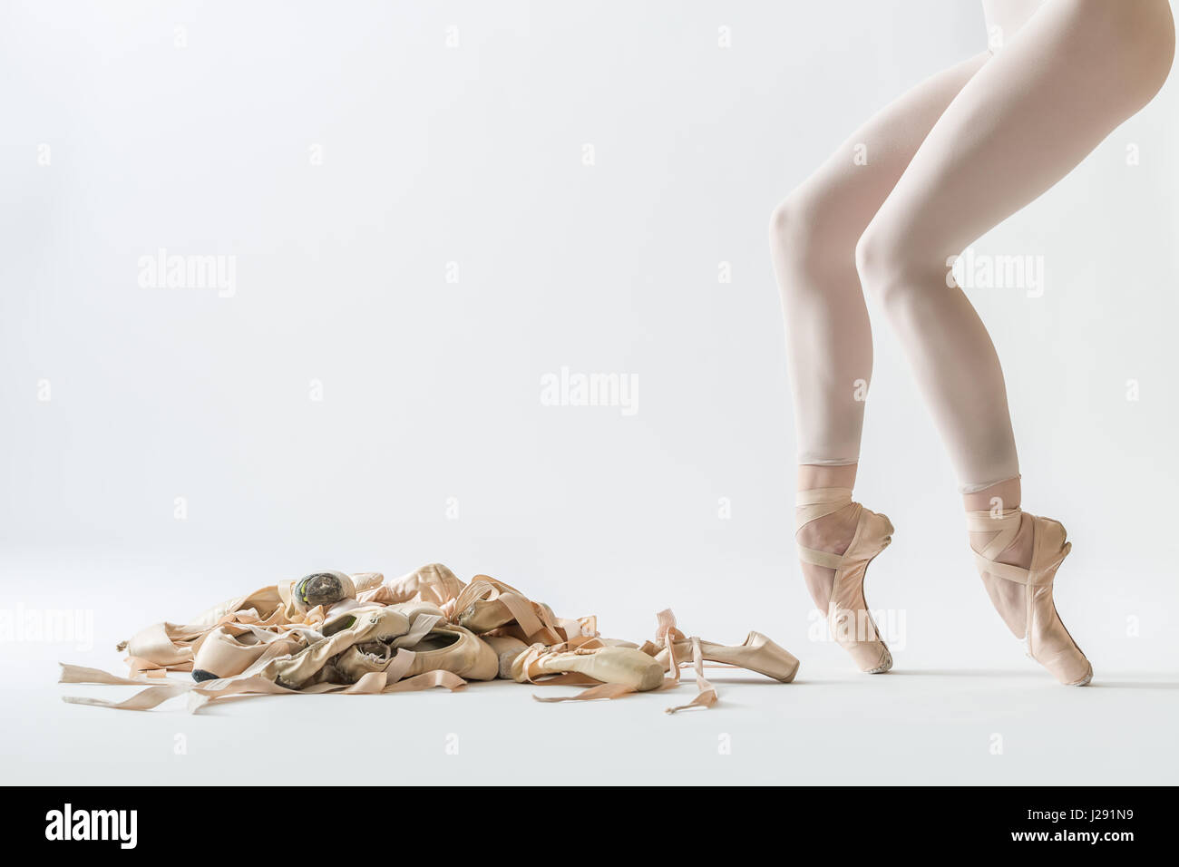Many beige pointe shoes on the light background in the studio. Next to it  there are ballerina's legs on the pointes in beige dance wear. Closeup.  Hori Stock Photo - Alamy