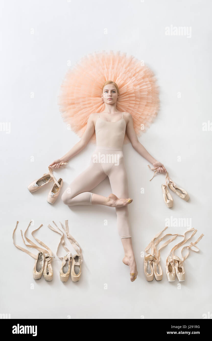 Tender ballerina lies in passe on the peach tutu on the white floor and ...