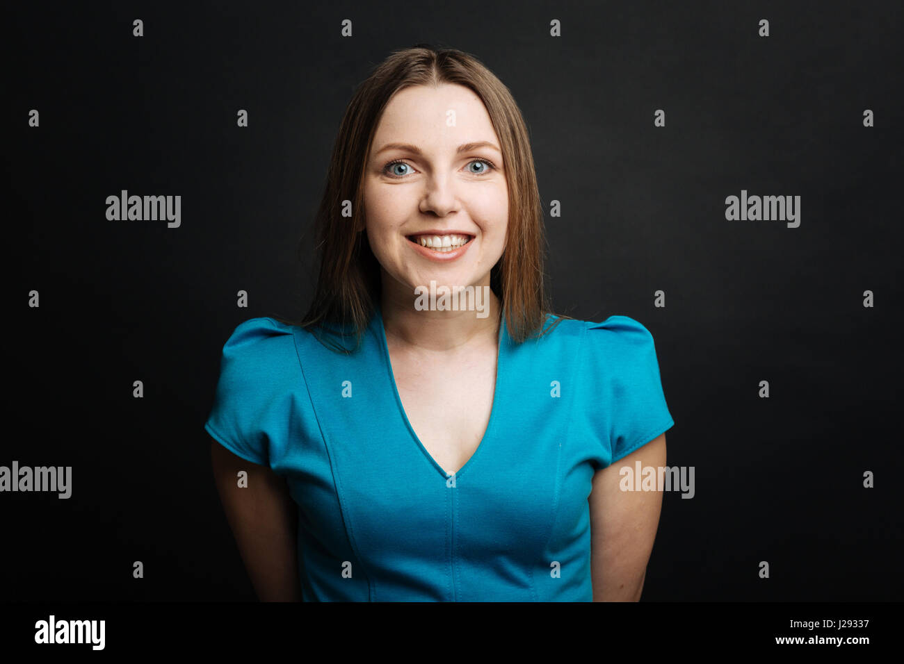 Cheerful young woman smiling in the black colored studio Stock Photo