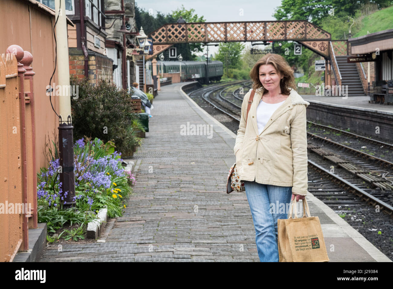 Woman standing on a vintage railway platform carrying a hessian Stock Photo