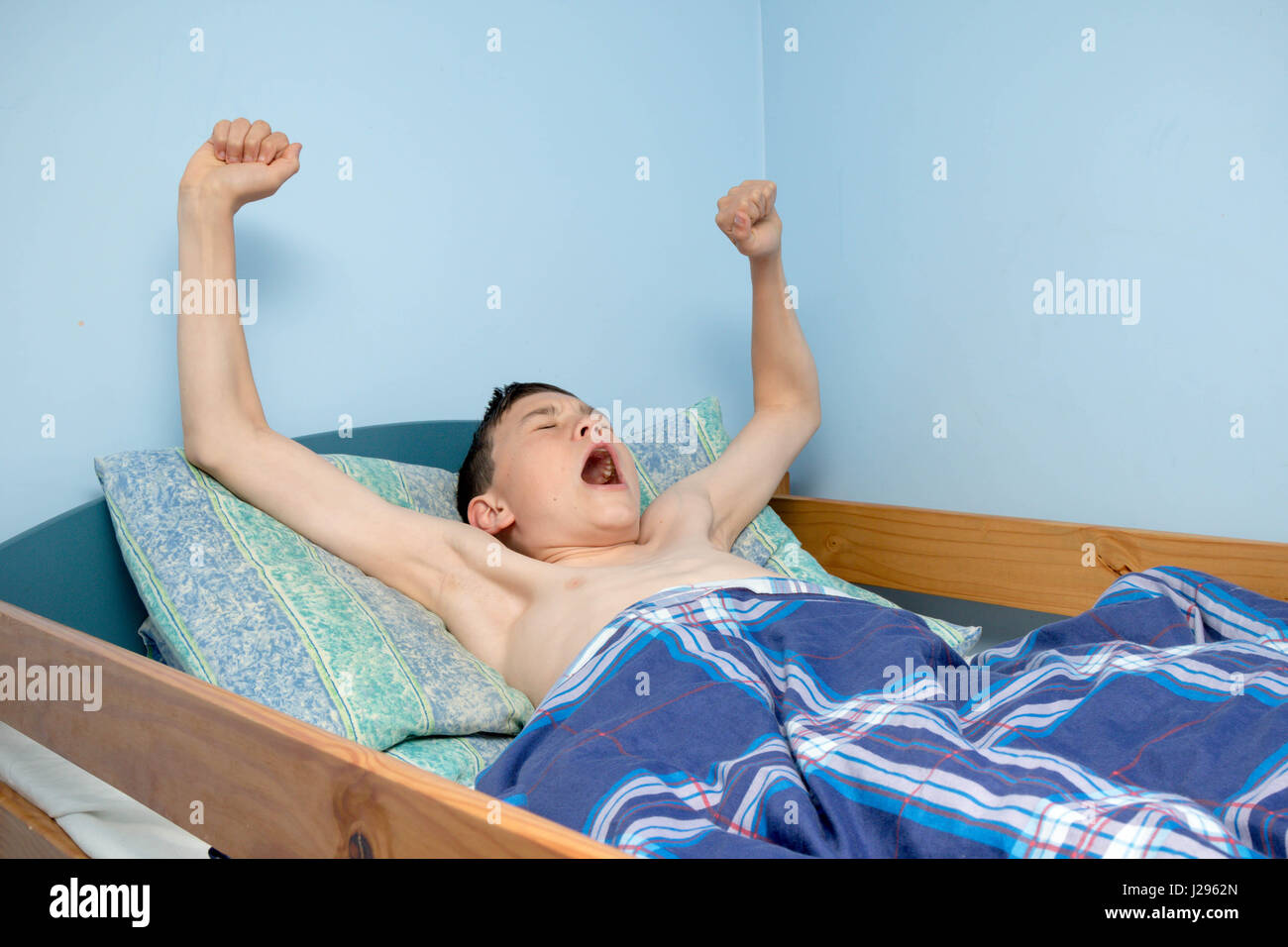 Young caucasian teenage boy waking up in bed Stock Photo
