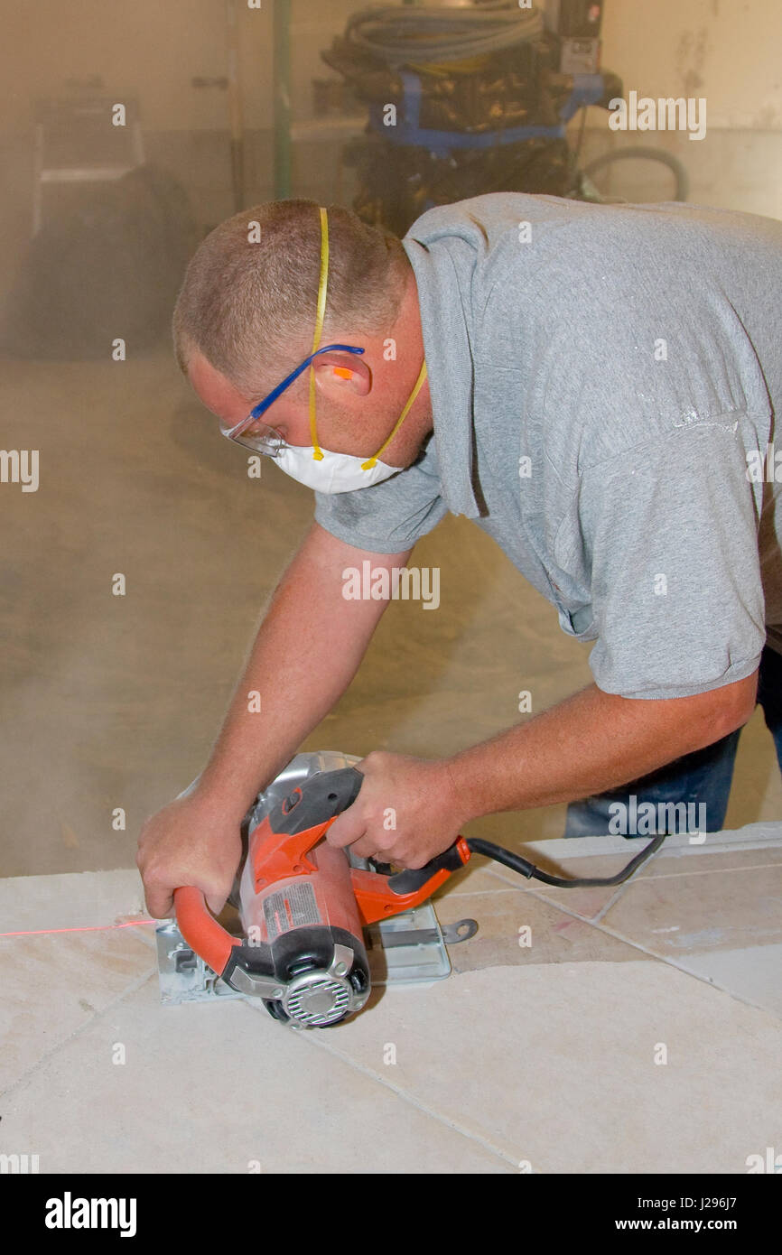 Carpenter cutting ceramic tile to prepare flloor base for new wall
