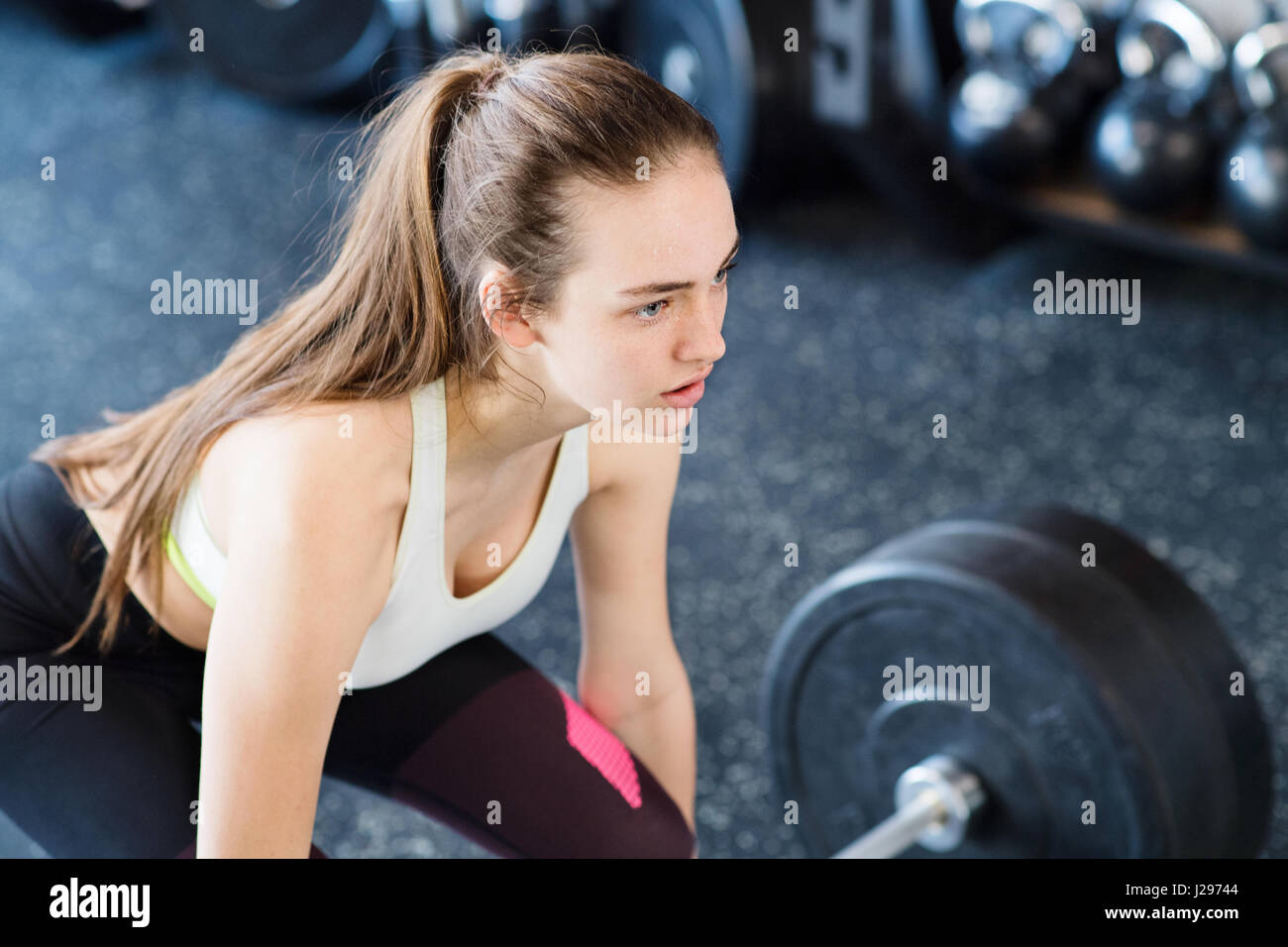 Beautiful young fit woman in gym lifting heavy barbell, flexing muscles Stock Photo