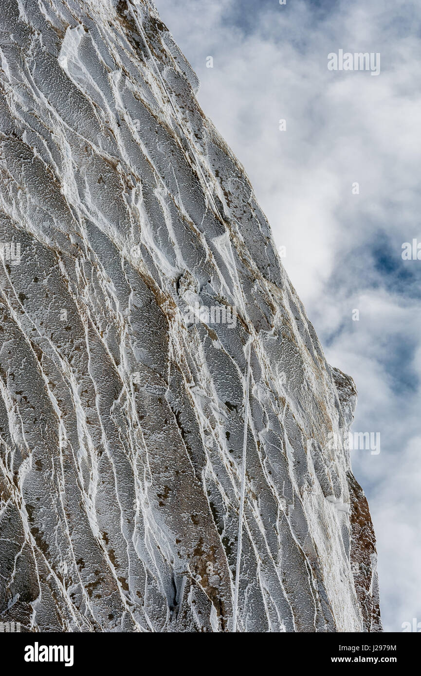 Ice crystals and surface hoar formed from overnight freeze on high alpine rockface in winter against partly cloud covered sky Stock Photo