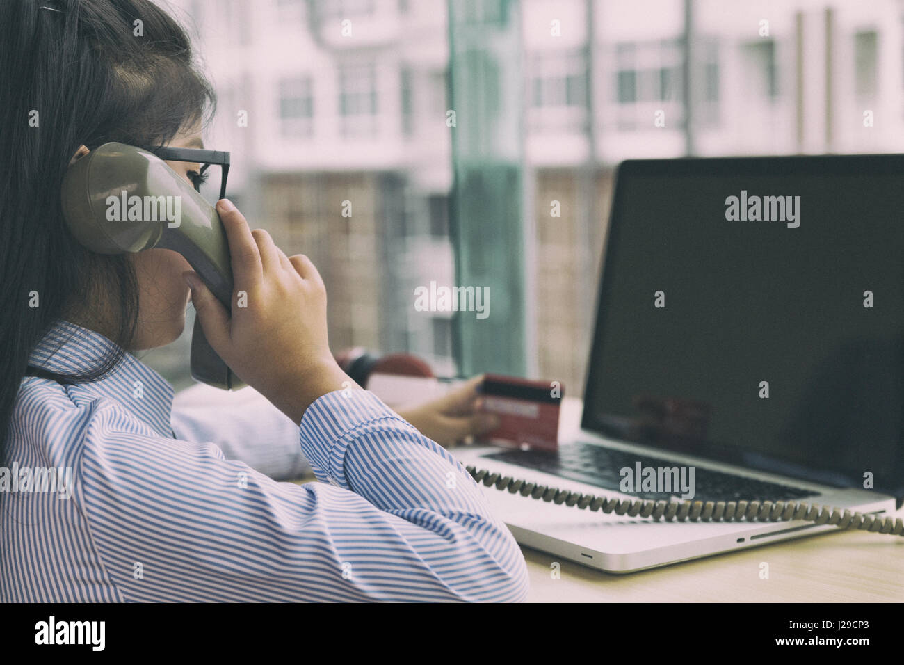 young asian girl holding credit card, making call, using telephone, talking on phone and using laptop computer for purchasing from internet. online sh Stock Photo