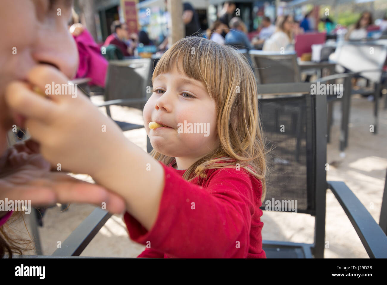 blonde three years old child, with red shirt, feeding mother with