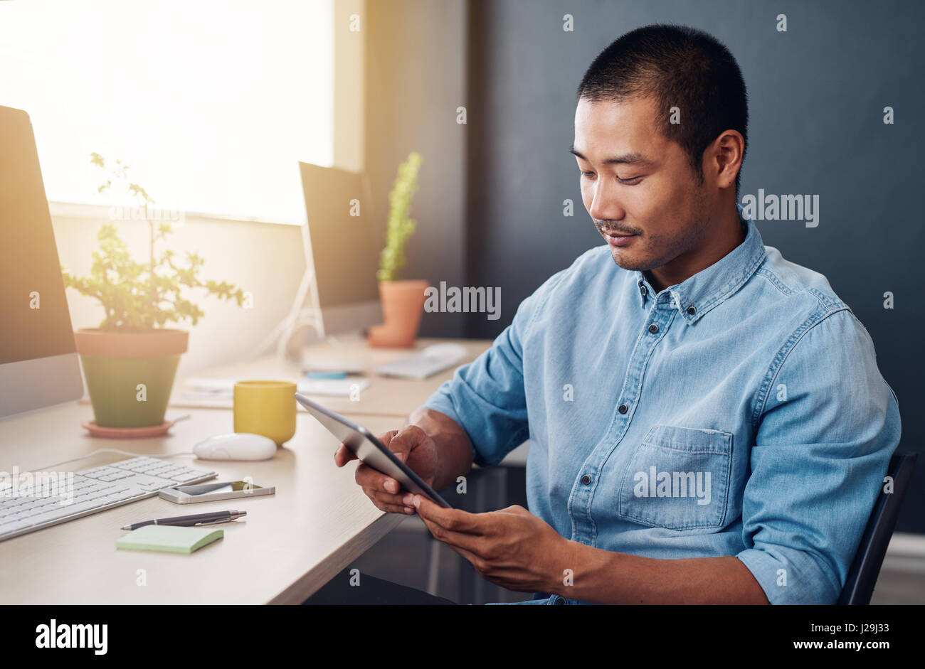 Focused Asian designer using a digital tablet at his desk Stock Photo