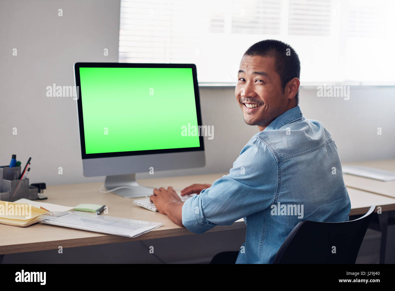 Smiling young Asian designer at work on an office computer Stock Photo