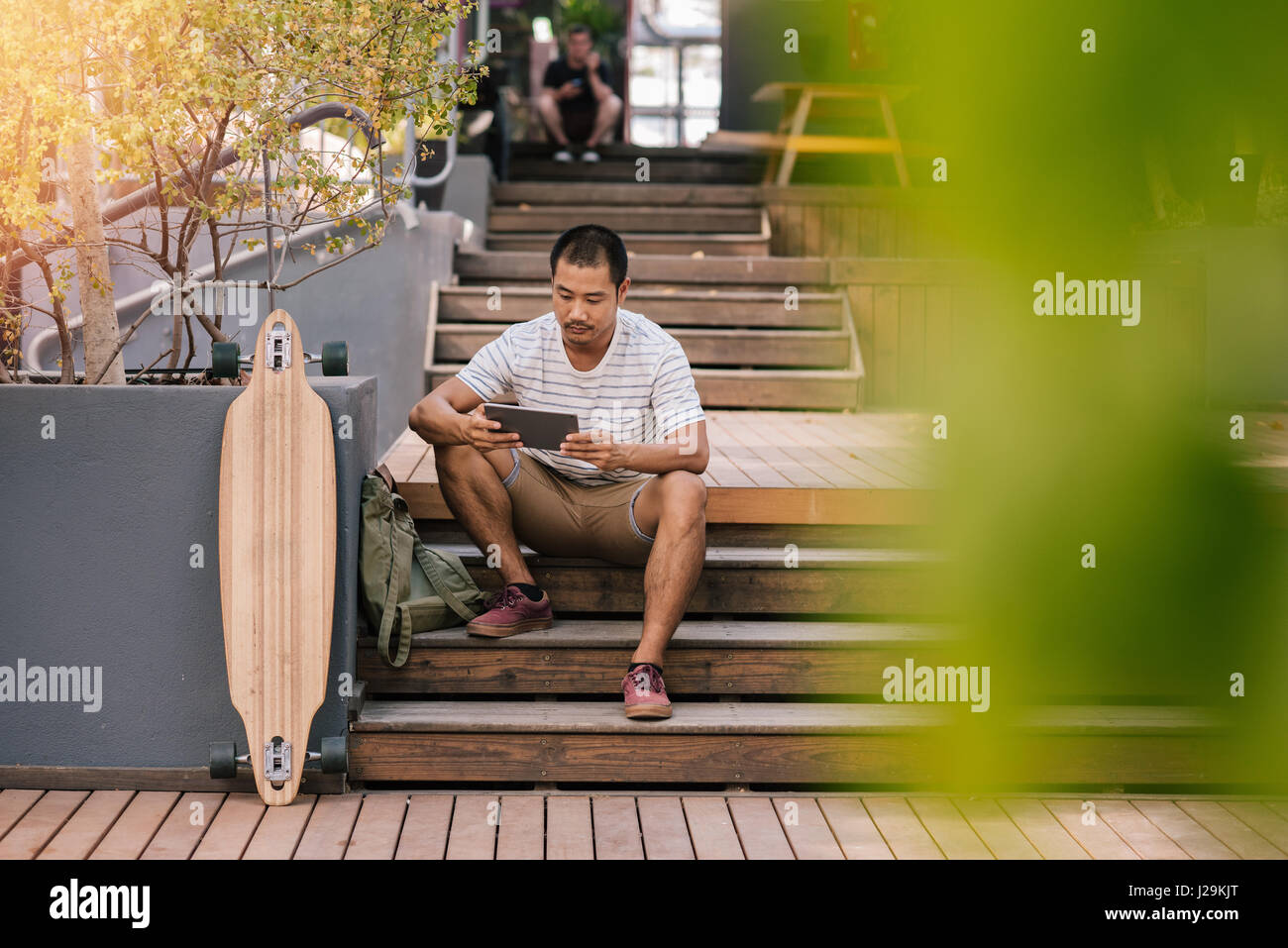 Young Asian man sitting on stairs outside using a tablet Stock Photo ...