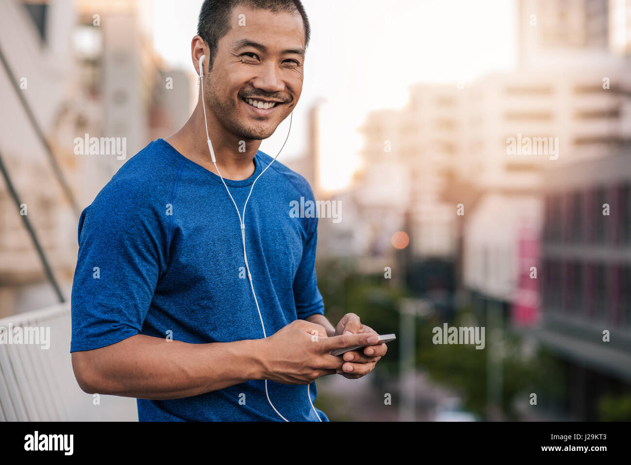 Smiling Asian man preparing a playlist for a city run Stock Photo