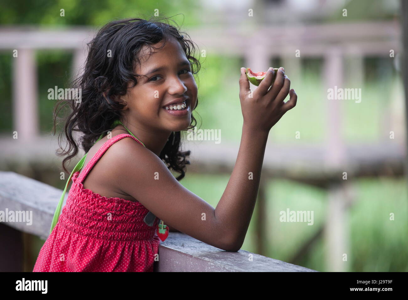 Brazil, Amapa, Smiling 8-year-old girl eating a mango Stock Photo