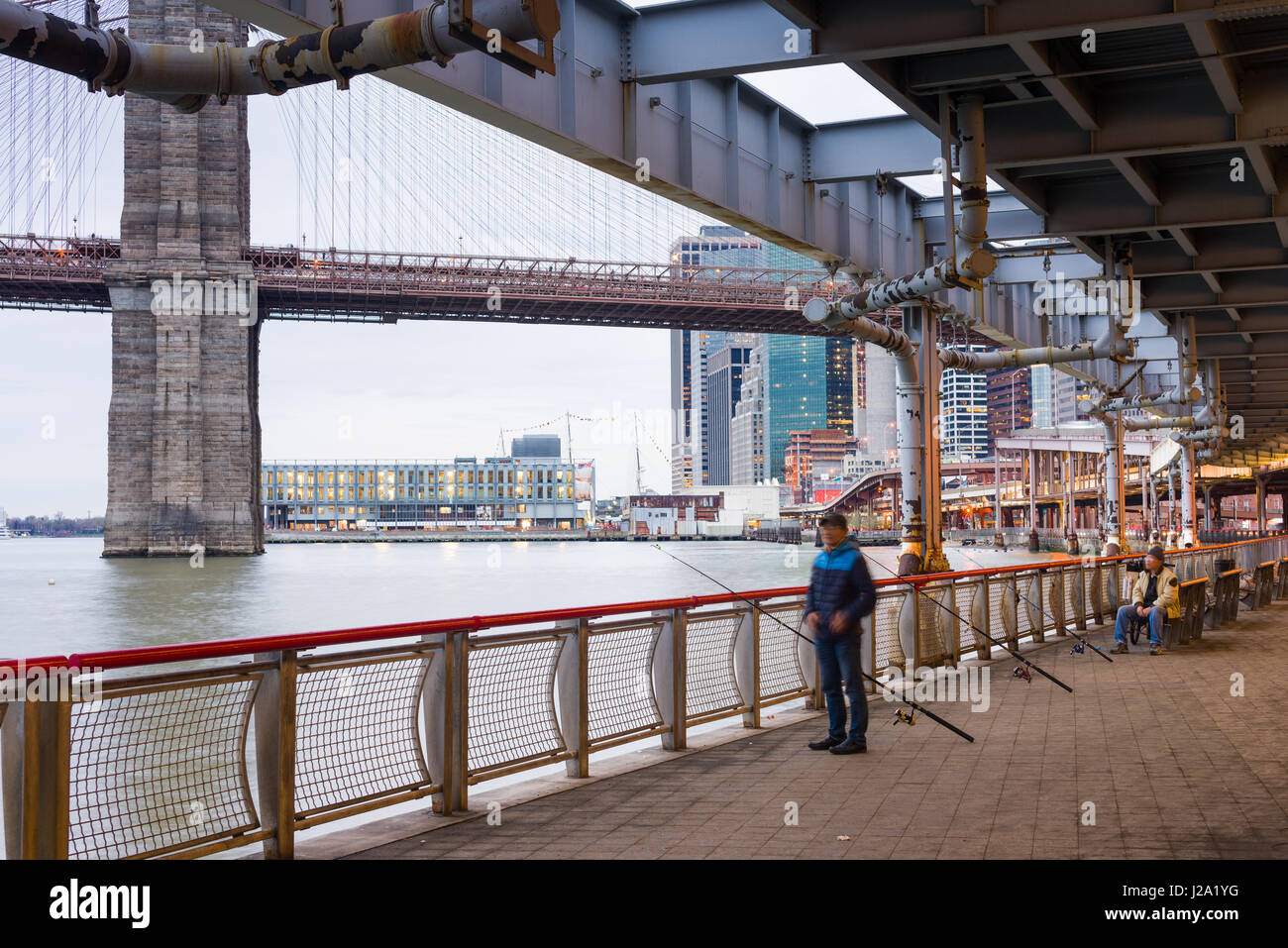 A Chinese Man Fishing In The East River Under FDR Drive And Brooklyn Bridge, New York Stock Photo