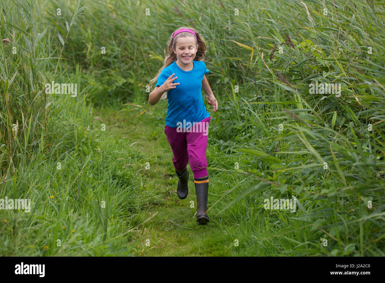 A little girl runs over a path through high reed, model released Stock Photo