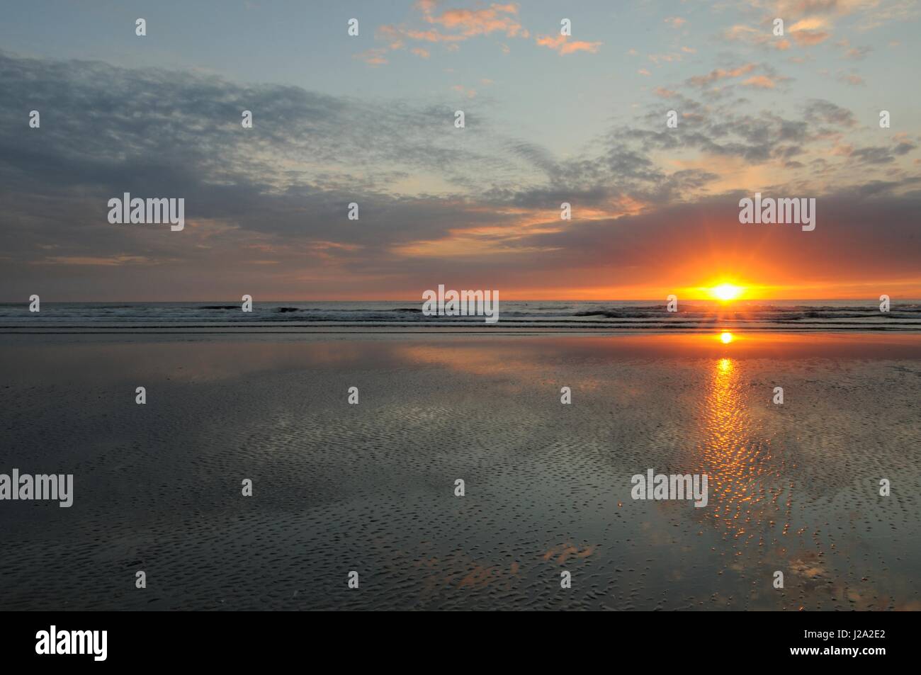 Last sunlight shining through under cloud during sunset on a warm summer evening on the beach of Wijk aan Zee Stock Photo