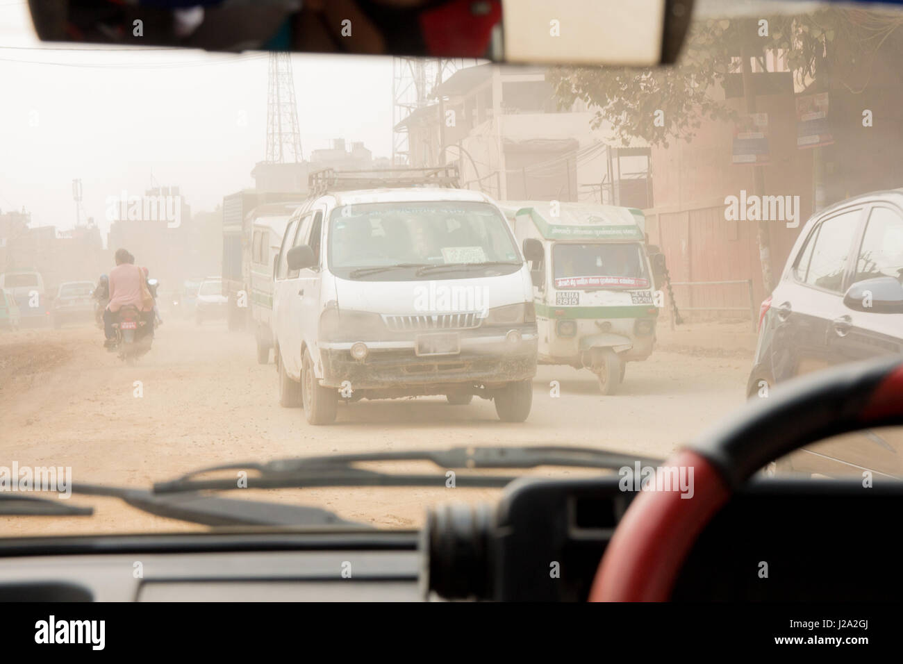 Traffic rushes through an extremely dusty and polluted i street in Kathmandu, Nepal. Shot from the inside of a small taxi car. Stock Photo