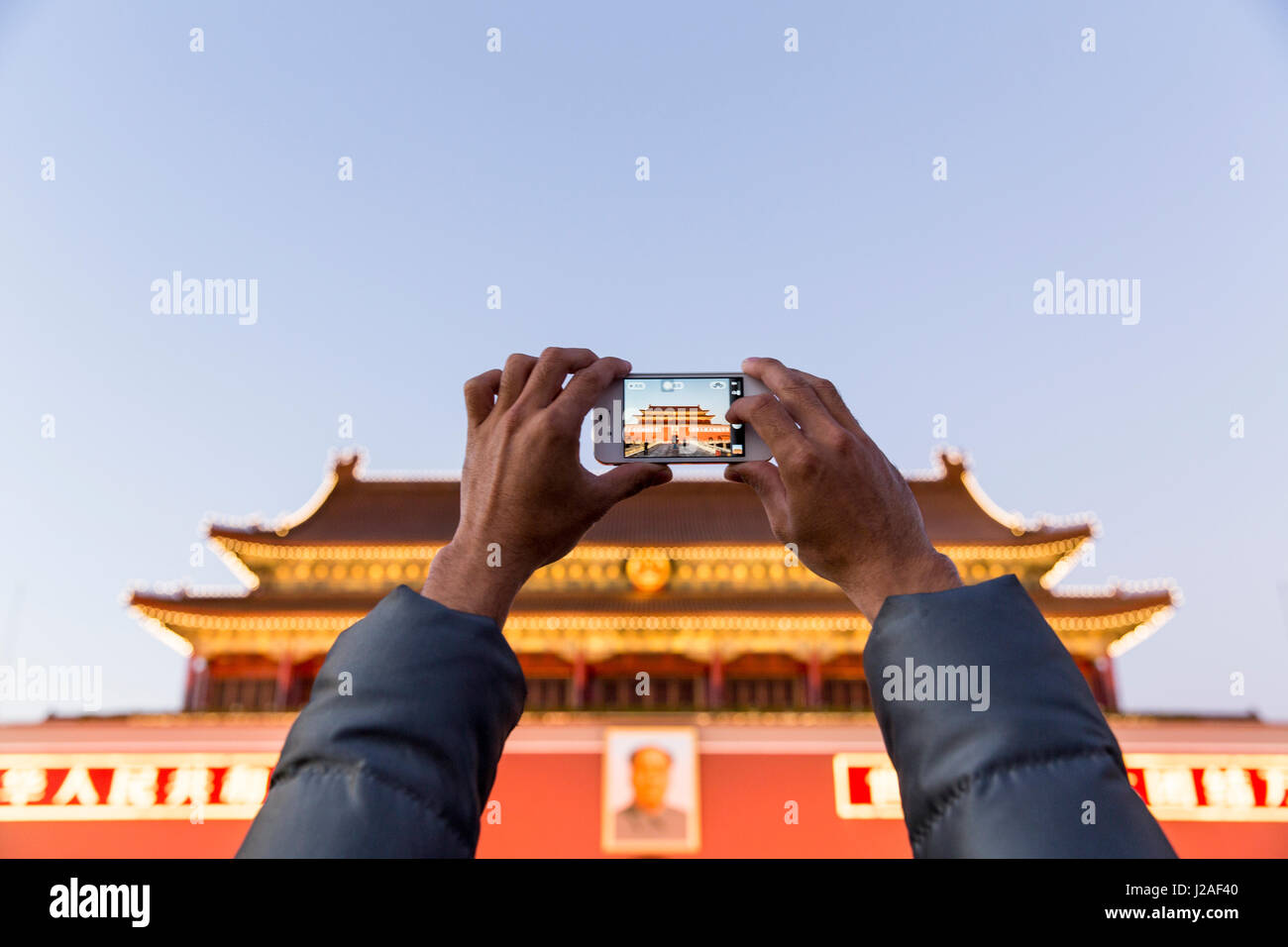 China, Beijing, Visitor takes snapshots with cellphone camera outside Gate of Heavenly Peace at Forbidden City by Tiananmen Square at dusk Stock Photo