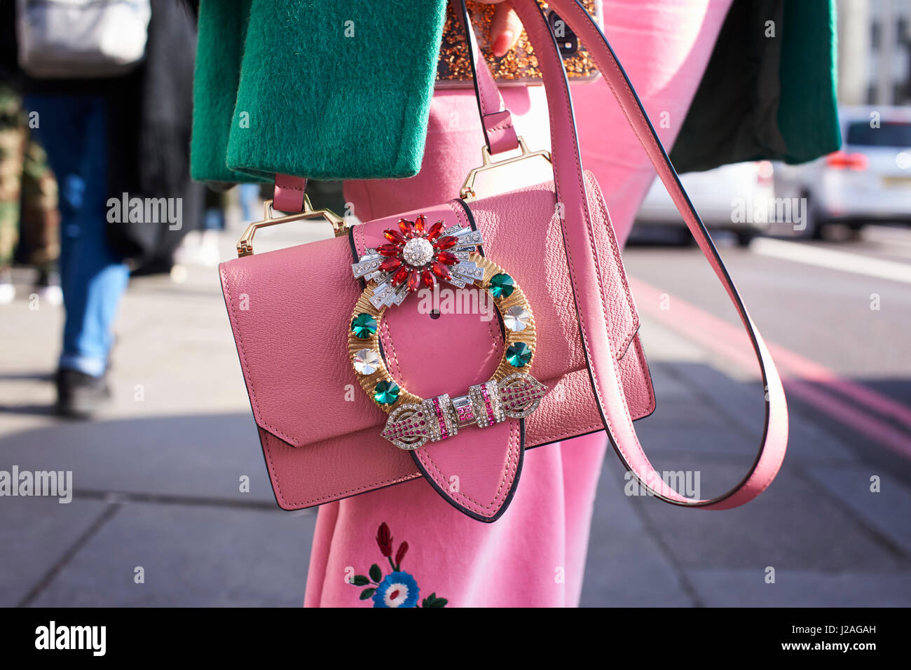 LONDON - FEBRUARY, 2017: Mid section of woman wearing pink skirt holding pink Miu Miu handbag and coat with floral decoration in street during London Fashion Week Stock Photo