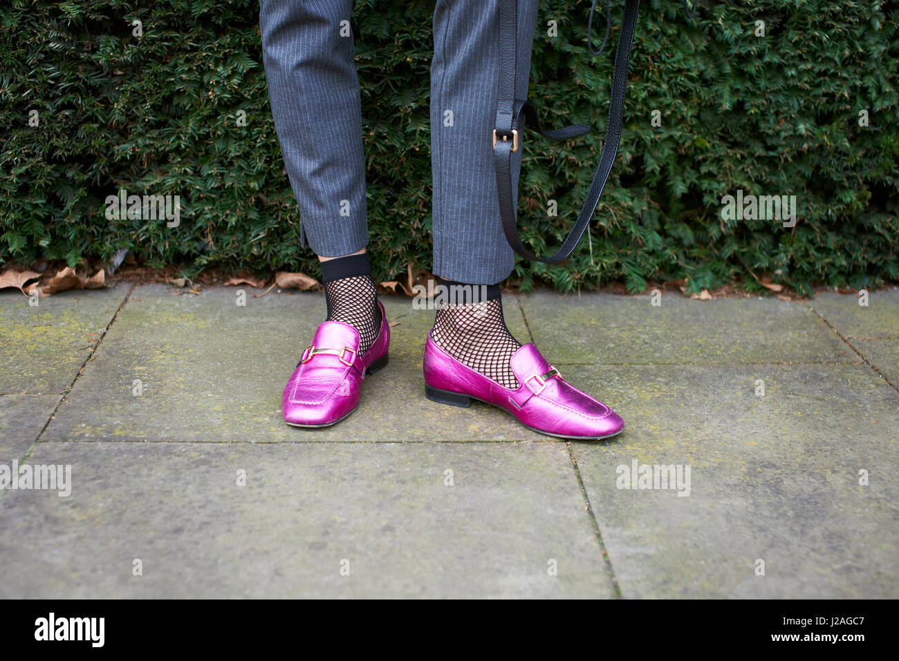 LONDON - FEBRUARY, 2017: Low section detail of woman standing in street wearing metallic pink loafer shoes, fishnet socks and trousers during London Fashion Week, horizontal Stock Photo