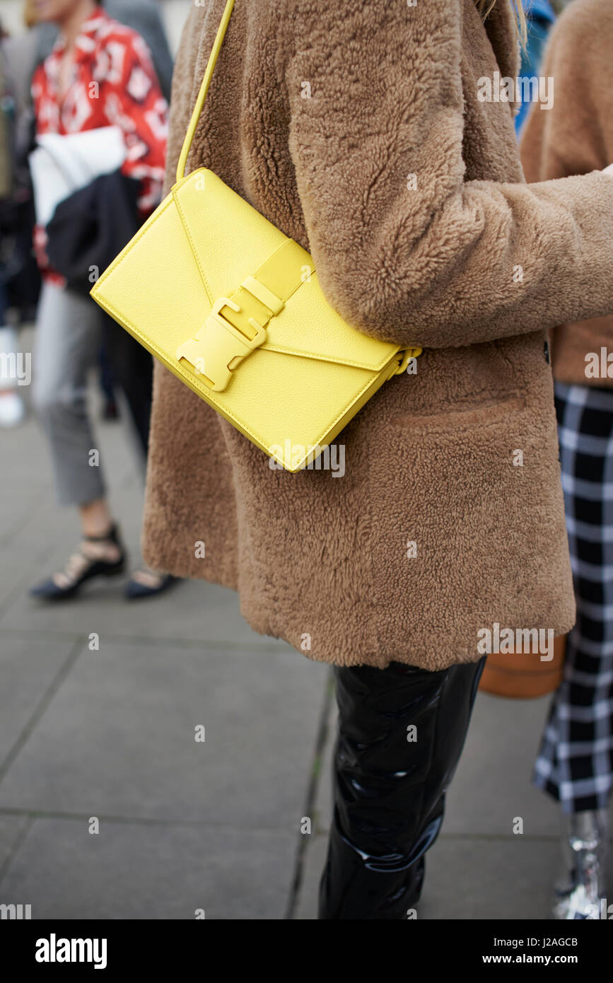 LONDON - FEBRUARY, 2017: Mid section of woman standing in street wearing short brown coat and yellow Christopher Kane handbag during London Fashion Week, vertical Stock Photo